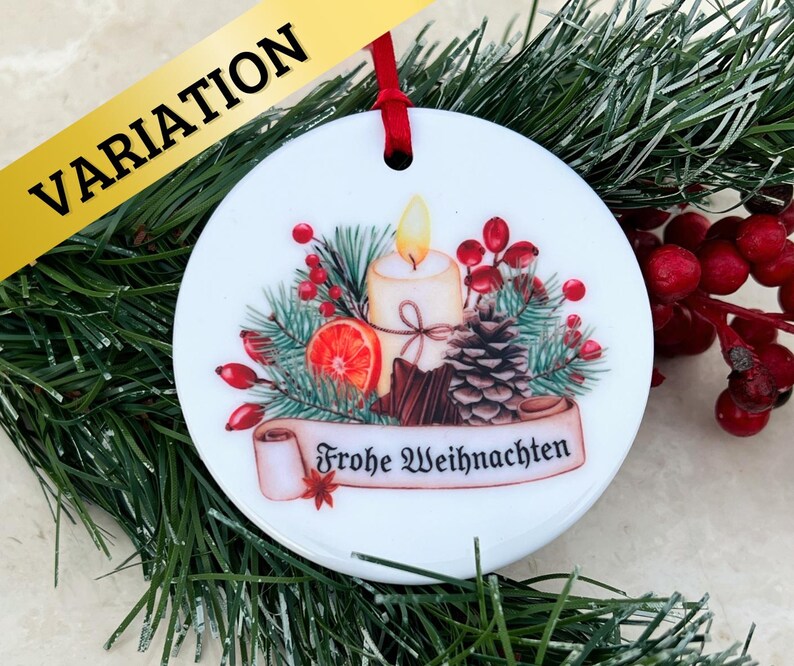 May include: White ceramic Christmas ornament with a festive design featuring a lit candle, pine branches, berries, and a scroll with the text "Frohe Weihnachten".