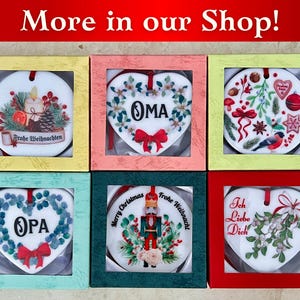 May include: Six heart-shaped ceramic ornaments in individual boxes. The ornaments feature various Christmas-themed designs, including a Christmas tree, a nutcracker, a heart with the word "OMA", a heart with the word "OPA", a heart with the words "Ich Liebe Dich", and a heart with the words "Frohe Weihnachten".