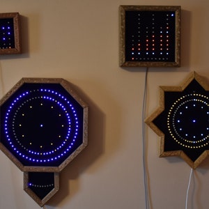 May include: Four illuminated wall art pieces with wooden frames are displayed. The pieces showcase geometric shapes: a rectangle, square, octagon, and star. Each has embedded LED lights in blue, red, and white, forming patterns. The frames are a warm, natural wood tone.