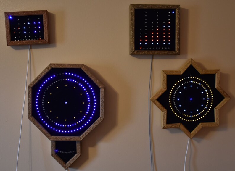 May include: Four illuminated wall art pieces with wooden frames are displayed. The pieces showcase geometric shapes: a rectangle, square, octagon, and star. Each has embedded LED lights in blue, red, and white, forming patterns. The frames are a warm, natural wood tone.
