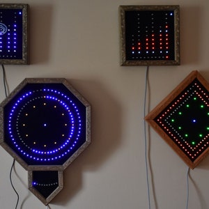 May include: Several framed LED light displays in different shapes, including square, octagonal, and rectangular. The lights are arranged in patterns, with blue, red, green, and white colours. The frames have ornate, gold-coloured edges and are mounted on a neutral wall.