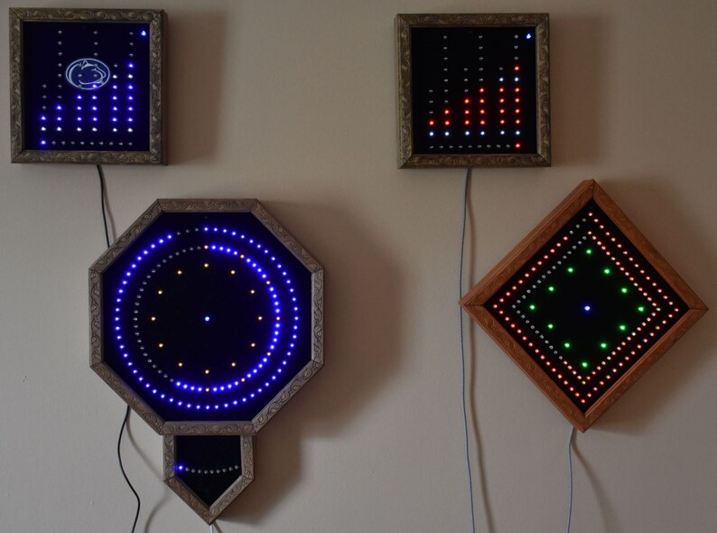 May include: Several framed LED light displays in different shapes, including square, octagonal, and rectangular. The lights are arranged in patterns, with blue, red, green, and white colours. The frames have ornate, gold-coloured edges and are mounted on a neutral wall.