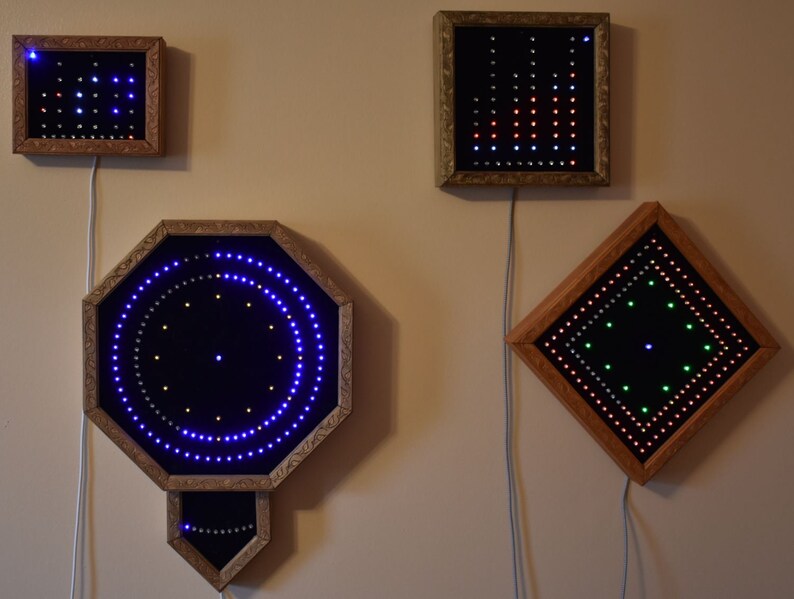 May include: Four framed LED light displays with wooden frames. The displays are various shapes, including a square, rectangle, octagon, and diamond. The lights are blue, green, red, and white, creating patterns. Each display is connected to a power source.