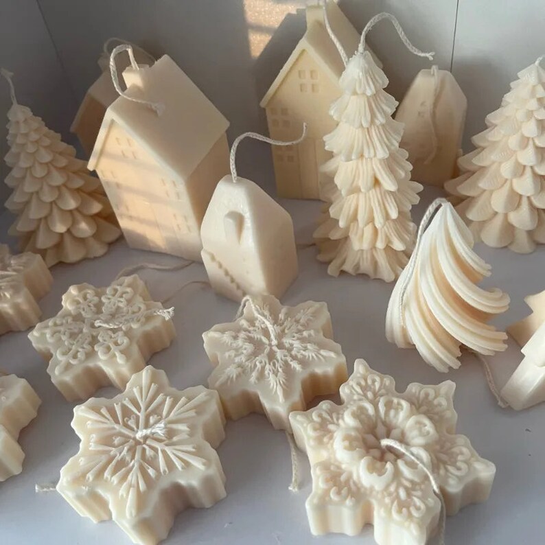 May include: A collection of white, hand-poured candles in various shapes, including houses, trees, and snowflakes. The candles are made of natural soy wax and have a delicate, frosted finish.