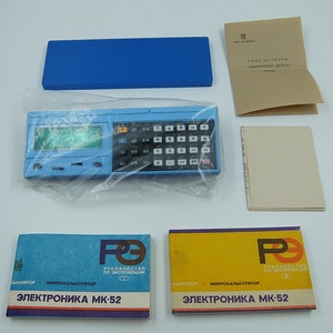 Può includere: Una calcolatrice blu e nera con uno schermo di visualizzazione e una tastiera. La calcolatrice è etichettata "Электроника МК-52" e viene fornita con due manuali di istruzioni.