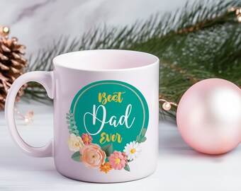 Könnte beinhalten: Hellrosa Keramiktasse mit dem Schriftzug "Best Dad Ever" in weißer Schrift in einem türkisfarbenen Kreis, verziert mit floralen Akzenten. Die Tasse hat einen weißen Henkel und einen unscharfen Hintergrund.