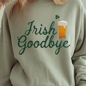 May include: A white ceramic mug with a black handle and the text "But First, Coffee" in a bold, black font. The mug is set against a blurred background. The mug appears to be approximately 10 cm tall.