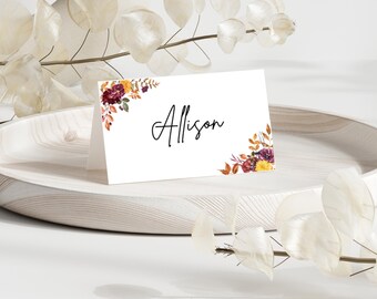 May include: A white place card with a floral design in shades of red, orange, and yellow. The name "Allison" is written in black calligraphy.