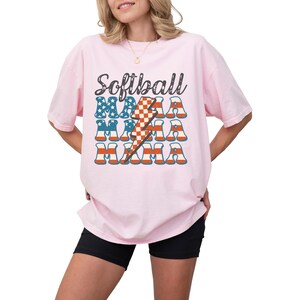 Retro patriotic softball mama shirt for 4th of July and Memorial day. The t shirt says, softball in black distressed script and the word mama repeated 3 times in a red white and blue USA flag font. A checkered lightning bolt down the middle