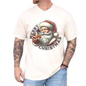 Christmas drinking shirt graphic tee. The t shirt has a distressed, vintage Santa that is holding a glass of whiskey or bourbon on the rocks. The tshirt says Merry Christmas. Comfort Colors tee, short sleeves, crewneck