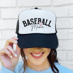 May include: A black and white trucker hat with a white mesh back. The front of the hat has the text "Baseball Mama" in black with a red and white baseball graphic.