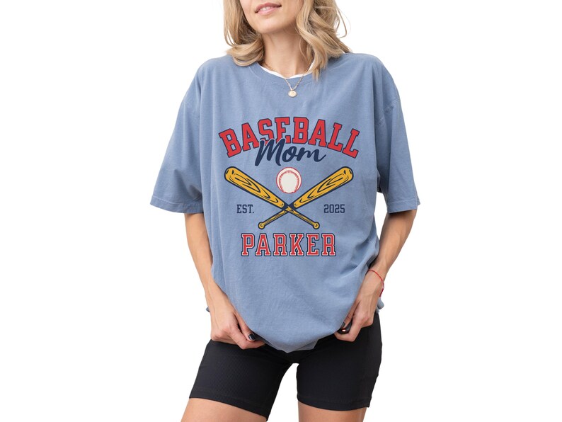 baseball mom shirt. the baseball mom tee says baseball mom and is personalized with the player name and the year. The graphic has two baseball bats and a baseball. comfort colors, short sleeves, crewneck, baseball tshirt for mama