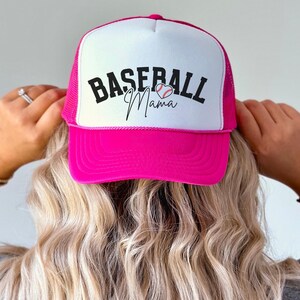 May include: Pink and white baseball cap with a black and white baseball graphic and the text "Baseball Mama" in black.
