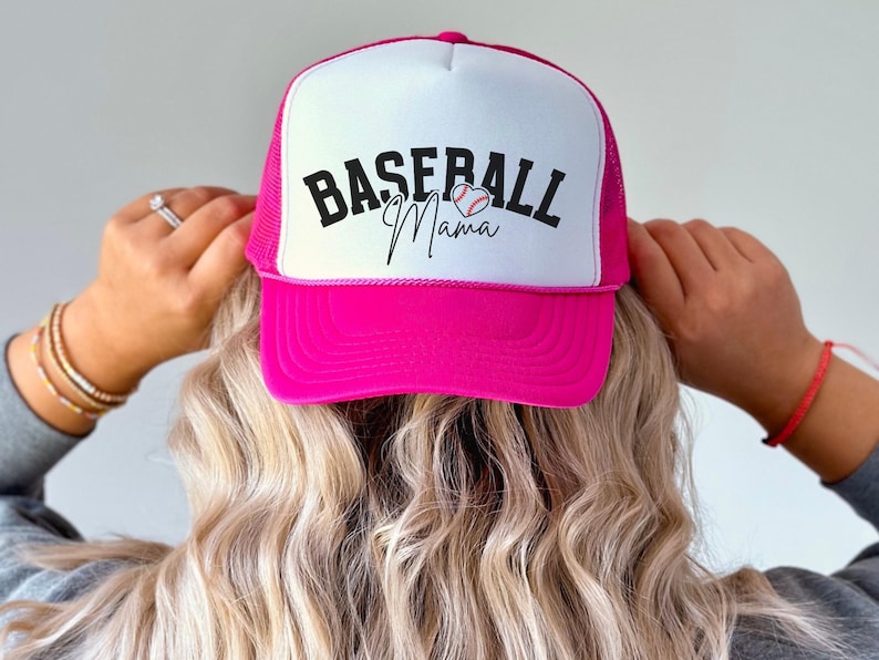 May include: Pink and white baseball cap with a black and white baseball graphic and the text "Baseball Mama" in black.