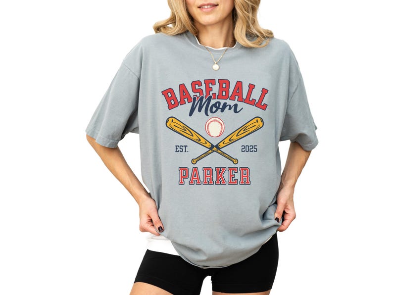 baseball mom shirt. the baseball mom tee says baseball mom and is personalized with the player name and the year. The graphic has two baseball bats and a baseball. comfort colors, short sleeves, crewneck, baseball tshirt for mama