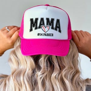 Custom baseball mom hat. the baseball hat says mama and has a baseball shaped heart in the center. the baseball mom trucker hat is personalized with the player name and number. adjustable, mesh back, baseball trucker hat