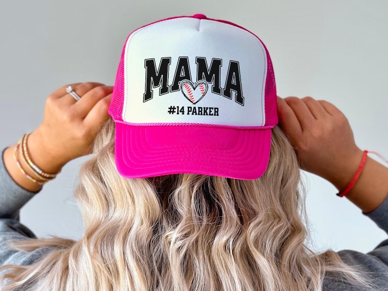 Custom baseball mom hat. the baseball hat says mama and has a baseball shaped heart in the center. the baseball mom trucker hat is personalized with the player name and number. adjustable, mesh back, baseball trucker hat