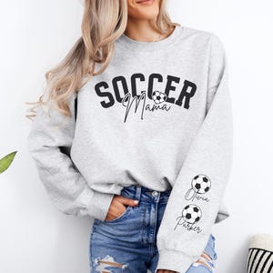 May include: Gray sweatshirt with the text "Soccer Mama" and a soccer ball graphic. The sleeves have soccer balls and the names "Olivia" and "Parker" written in cursive.