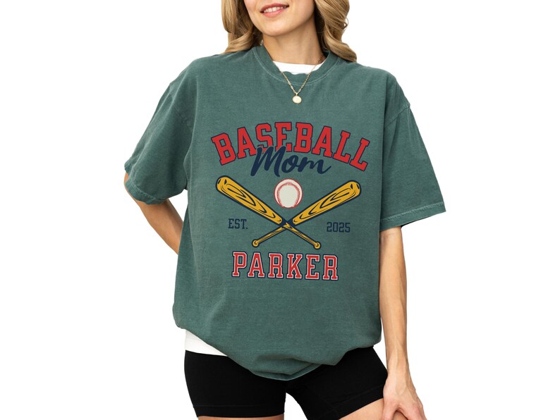 baseball mom shirt. the baseball mom tee says baseball mom and is personalized with the player name and the year. The graphic has two baseball bats and a baseball. comfort colors, short sleeves, crewneck, baseball tshirt for mama