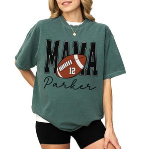 Custom Football Mama Shirt. The tshirt says football mama in varsity font and is personalized with the players number on a large football and name below it. Comfort Colors tee, crewneck, short sleeves football mom t shirt