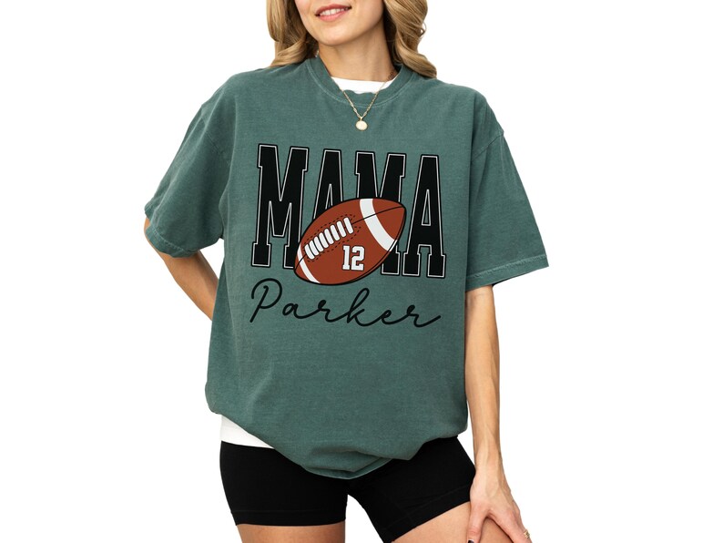 Custom Football Mama Shirt. The tshirt says football mama in varsity font and is personalized with the players number on a large football and name below it. Comfort Colors tee, crewneck, short sleeves football mom t shirt