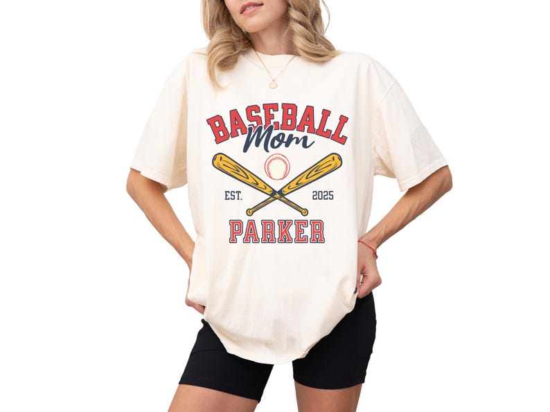 baseball mom shirt. the baseball mom tee says baseball mom and is personalized with the player name and the year. The graphic has two baseball bats and a baseball. comfort colors, short sleeves, crewneck, baseball tshirt for mama