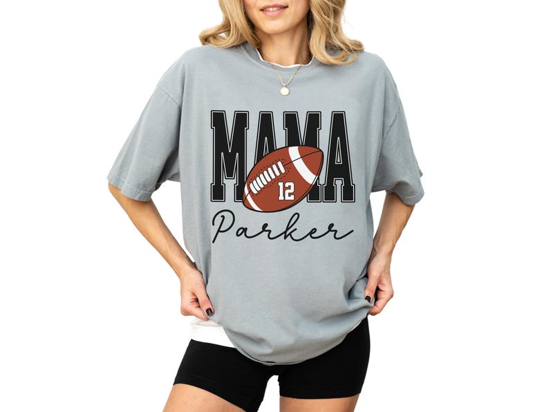 Custom Football Mama Shirt. The tshirt says football mama in varsity font and is personalized with the players number on a large football and name below it. Comfort Colors tee, crewneck, short sleeves football mom t shirt