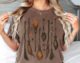 Könnte beinhalten: Braunes T-Shirt mit einem Design aus illustrierten Besen in verschiedenen Stilen. Das Design umfasst Sterne, Monde und ein Spinnennetz und schafft ein Halloween- oder Hexen-Thema. Das Shirt hat einen Vintage-Look.