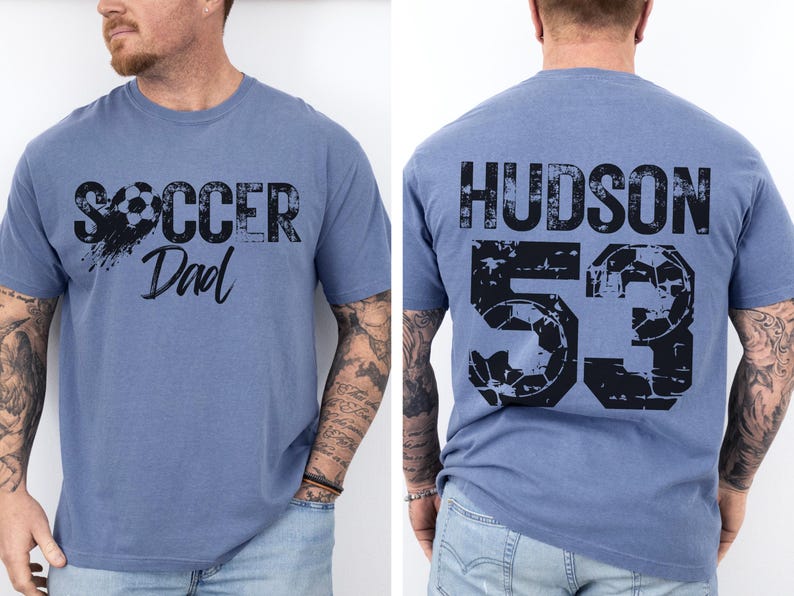 May include: A blue t-shirt with a distressed black graphic that says "Soccer Dad" on the front and "HUDSON 53" on the back.