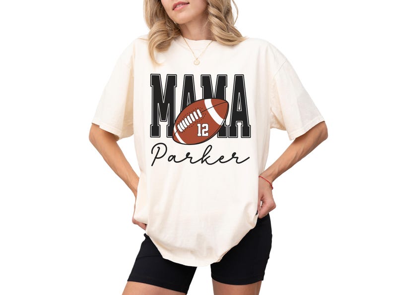 Custom Football Mama Shirt. The tshirt says football mama in varsity font and is personalized with the players number on a large football and name below it. Comfort Colors tee, crewneck, short sleeves football mom t shirt