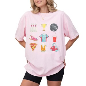 Retro bowling shirt for women. The tshirt has watercolor graphics and features bowling pins, trophy, bowling ball, shoes, shirt, soda, pizza, beer and a bowling bag. Short sleeves, crewneck, comfort colors, ivory