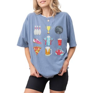 Retro bowling shirt for women. The tshirt has watercolor graphics and features bowling pins, trophy, bowling ball, shoes, shirt, soda, pizza, beer and a bowling bag. Short sleeves, crewneck, comfort colors, ivory