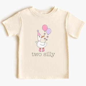 May include: Cream-colored toddler t-shirt featuring a cartoon goose wearing a party hat and boots, holding pink and purple balloons. The text "two silly" is printed below the goose.