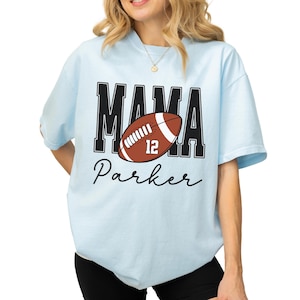Custom Football Mama Shirt. The tshirt says football mama in varsity font and is personalized with the players number on a large football and name below it. Comfort Colors tee, crewneck, short sleeves football mom t shirt