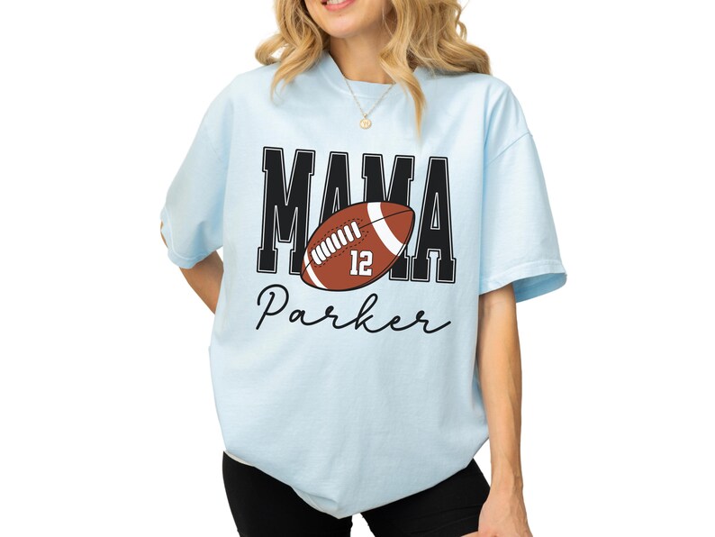 Custom Football Mama Shirt. The tshirt says football mama in varsity font and is personalized with the players number on a large football and name below it. Comfort Colors tee, crewneck, short sleeves football mom t shirt
