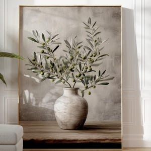 May include: A framed print of olive branches in a white vase, set against a neutral background. A potted plant and a footstool are in the foreground. Two terracotta vases and a small pot are on the right.