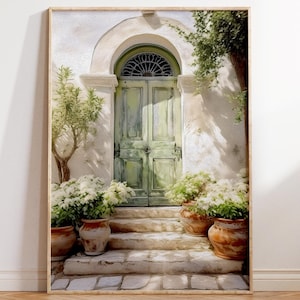 May include: Framed art print depicting a weathered green door with an arched top. The door is set into a white stucco wall, with stone steps leading up to it. Potted plants with white flowers and small trees flank the entrance.