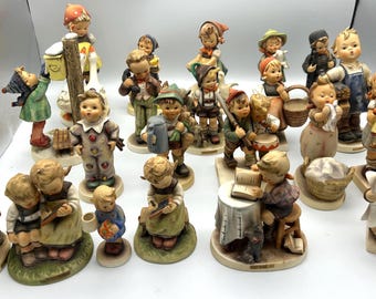 Op de afbeelding: Een verzameling vintage Hummel-beeldjes die kinderen in verschillende activiteiten uitbeelden. De beeldjes hebben gedetailleerde kleding en accessoires, met een reeks kleuren, waaronder blauw, groen en bruin. Elk beeldje is ongeveer 10 cm hoog.