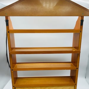 Pu&ograve; includere: Una mensola da parete in legno con un tetto a forma di casa e quattro ripiani. La mensola &egrave; realizzata in legno marrone chiaro e ha un piccolo cassetto in basso. Il design &egrave; semplice e funzionale, adatta per esporre piccoli oggetti.