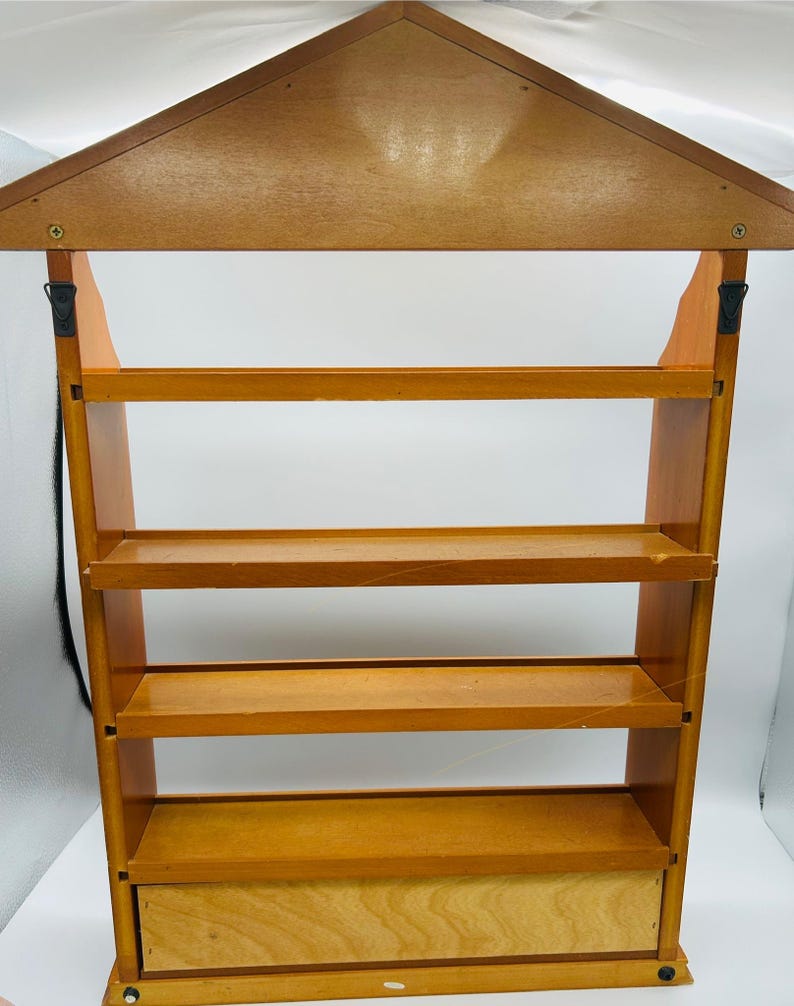 Pu&ograve; includere: Una mensola da parete in legno con un tetto a forma di casa e quattro ripiani. La mensola &egrave; realizzata in legno marrone chiaro e ha un piccolo cassetto in basso. Il design &egrave; semplice e funzionale, adatta per esporre piccoli oggetti.