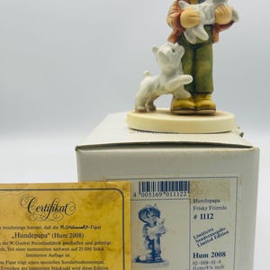 May include: A Hummel figurine titled "Hundepapa" (Hum 2008), depicting a young person holding a white dog, with another dog at their feet. The figurine is part of the "Frisky Friends" series, limited edition, and measures 4 3/8 inches.