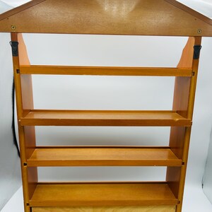 Pu&ograve; includere: Una mensola in legno con un tetto a forma di casa e quattro ripiani. L'unit&agrave; &egrave; realizzata in legno marrone chiaro e ha un piccolo cassetto in basso. I ripiani sono distanziati uniformemente e sembrano robusti.