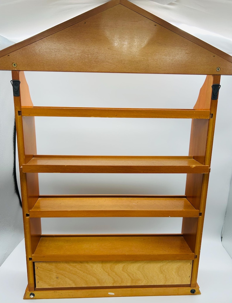 Pu&ograve; includere: Una mensola in legno con un tetto a forma di casa e quattro ripiani. L'unit&agrave; &egrave; realizzata in legno marrone chiaro e ha un piccolo cassetto in basso. I ripiani sono distanziati uniformemente e sembrano robusti.