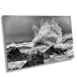 May include: A black and white photograph of a large wave crashing against rocky cliffs. The wave is breaking into a spray of water, creating a dramatic scene.