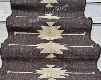 May include: A long, dark brown stair runner rug featuring a repeating cream-colored geometric star pattern centered along the length. The woven textile has a textured appearance and is draped over a set of white marble stairs, displaying the text Floor And Rugs.
