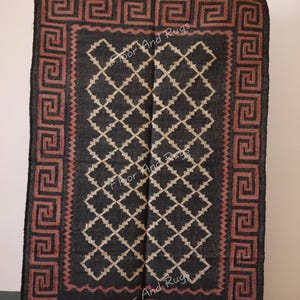 May include: Black and cream patterned rug with a red and black border featuring a Greek key design. The rug has fringe on the bottom edge.
