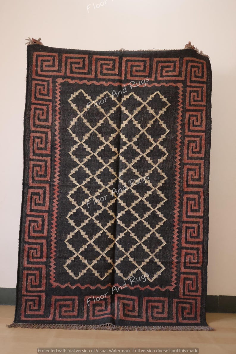 May include: Black and cream patterned rug with a red and black border featuring a Greek key design. The rug has fringe on the bottom edge.