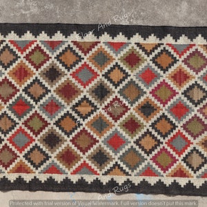 May include: A rectangular woven rug featuring a repeating diamond pattern in shades of red, brown, olive green, gray, and black. The rug is framed by a jagged, off-white border and a solid black outer edge, creating a geometric design.