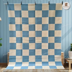 May include: A rectangular area rug featuring a repeating checkered pattern of alternating light blue and off-white squares. The rug is displayed hanging vertically, showcasing a consistent grid design across its entire surface area.