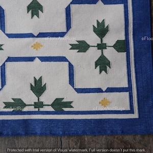 May include: A rectangular rug featuring a white background with a repeating geometric pattern in blue, dark green, and yellow. The design consists of blue linear borders framing dark green leaf-like motifs and small yellow diamond accents.